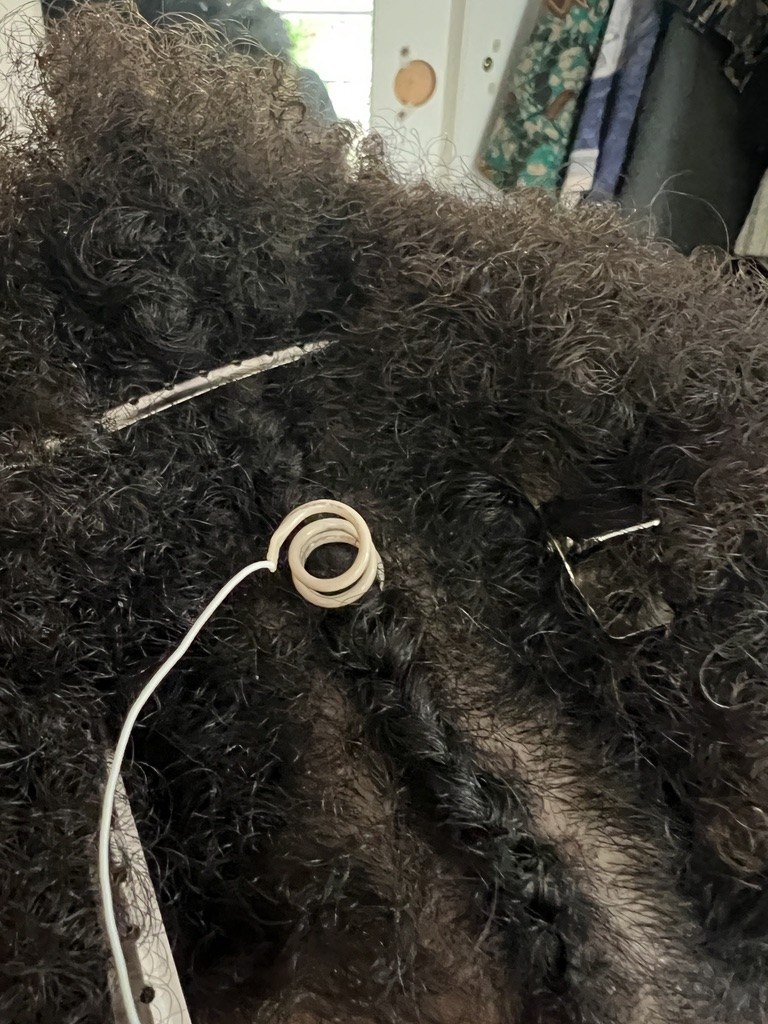 A Syn-R1 electrode seated in afro-textured hair, its spring tip reaching the scalp, with a standard clip and a cup electrode placed alongside it